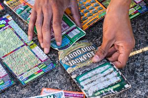 Hands scratching a $4,000,000 jackpot lottery ticket surrounded by multiple colorful scratch-off tickets on a surface.