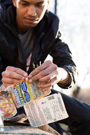 Young man scratching a Lucky Numbers lottery ticket outdoors on a sunny day.