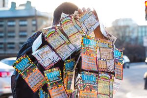 Person holding numerous scratch-off lottery tickets fanned out, covering their face, outdoors on a city street.