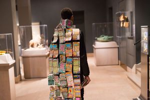 Person wearing a cape covered in lottery scratch tickets stands in a museum gallery.