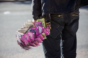Close-up of hands holding fan of colorful lottery scratch tickets outdoors.