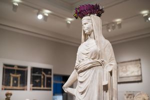 White marble statue of a Roman woman wearing a floral crown displayed in a museum gallery.