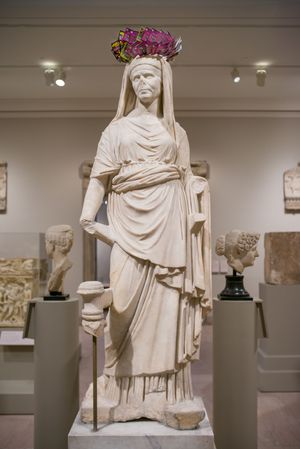 Ancient Roman marble statue of a draped female figure wearing a colorful floral crown, displayed in a museum gallery.