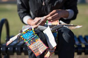 Person scratching lottery tickets on a park bench with multiple used scratch cards visible outdoors.