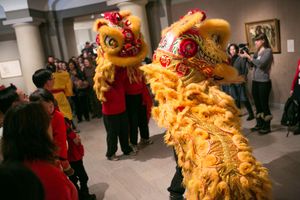 Golden lion dance costume performed indoors at a Chinese New Year celebration with spectators watching and photographing.
