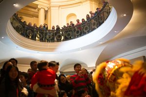 Crowd gathers in ornate rotunda balcony watching colorful cultural lion dance performance below.