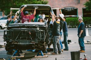 Group of people collaboratively dismantling a damaged vehicle in an urban parking lot during daytime.