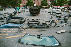 Disassembled car parts scattered across a parking lot, including bumpers, windshields, and panels.