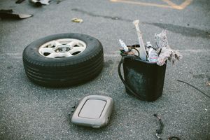 A spare tire, GPS device, and bucket filled with debris discarded on asphalt pavement.
