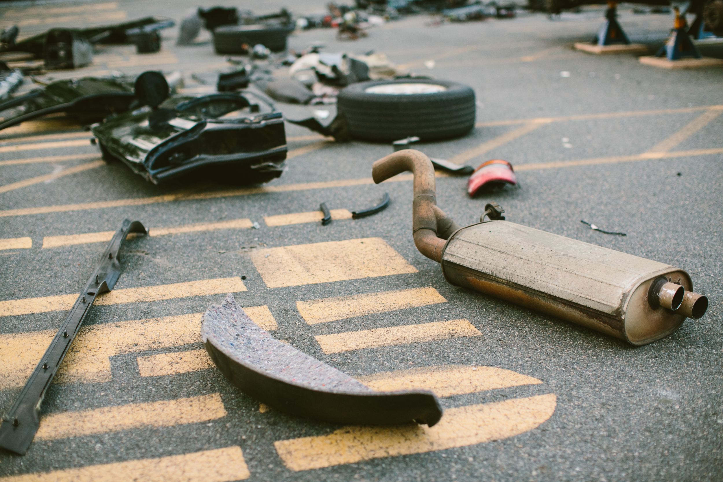 Scattered car parts including exhaust pipe and debris on asphalt parking lot surface.