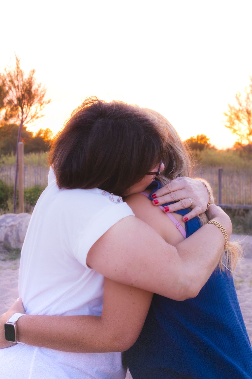 Two women sharing a warm embrace outdoors at sunset, with golden light and trees in the background.