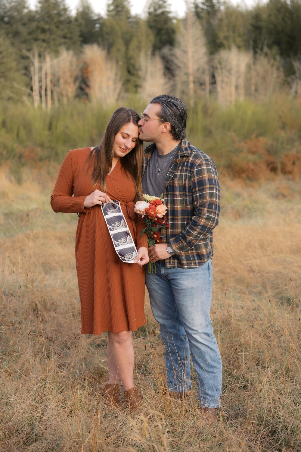 Couple holding ultrasound photos and flowers in autumn field during pregnancy announcement photo shoot.