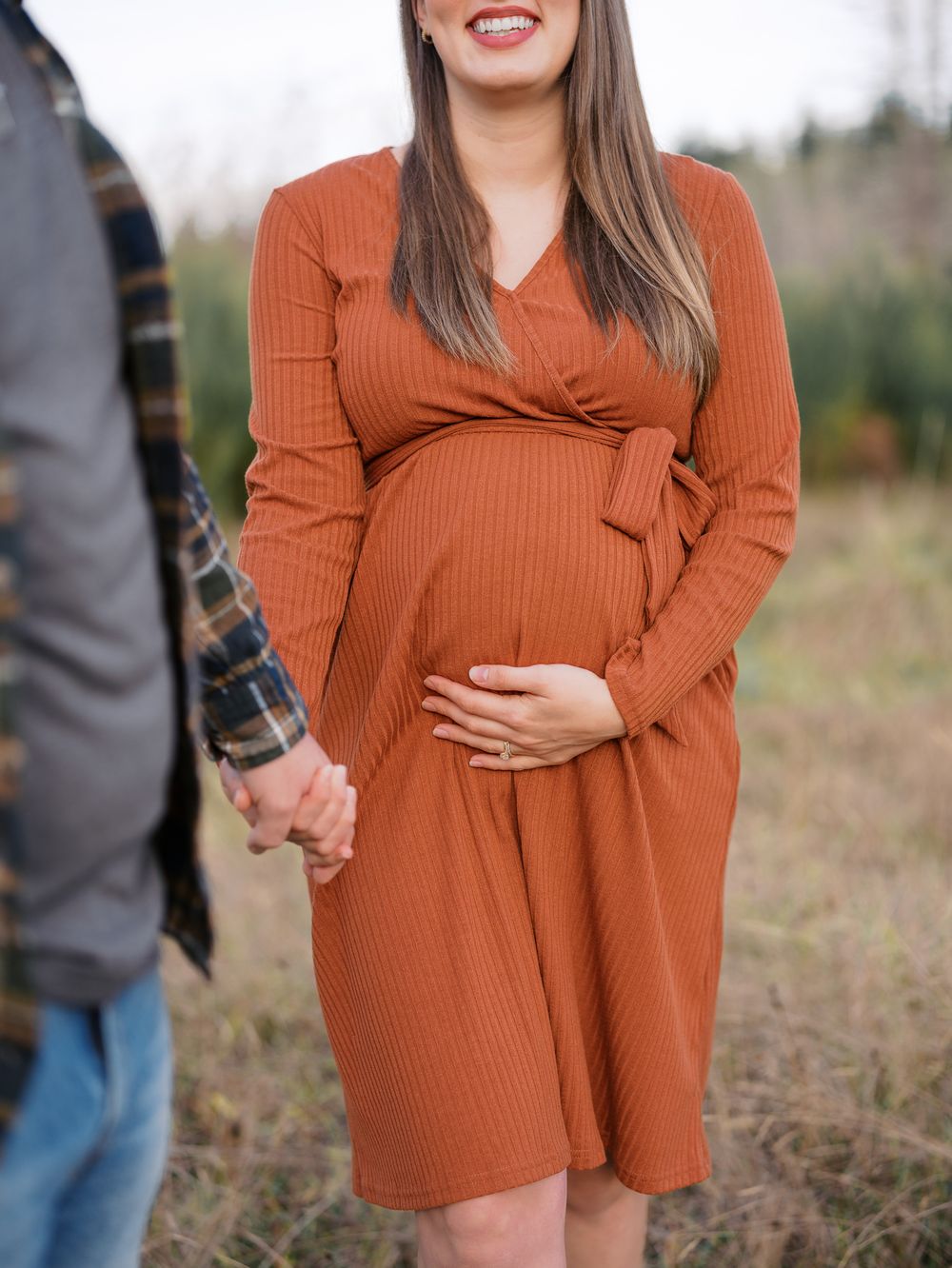 Pregnant woman in rust orange ribbed wrap dress holding baby bump outdoors during maternity photo session.