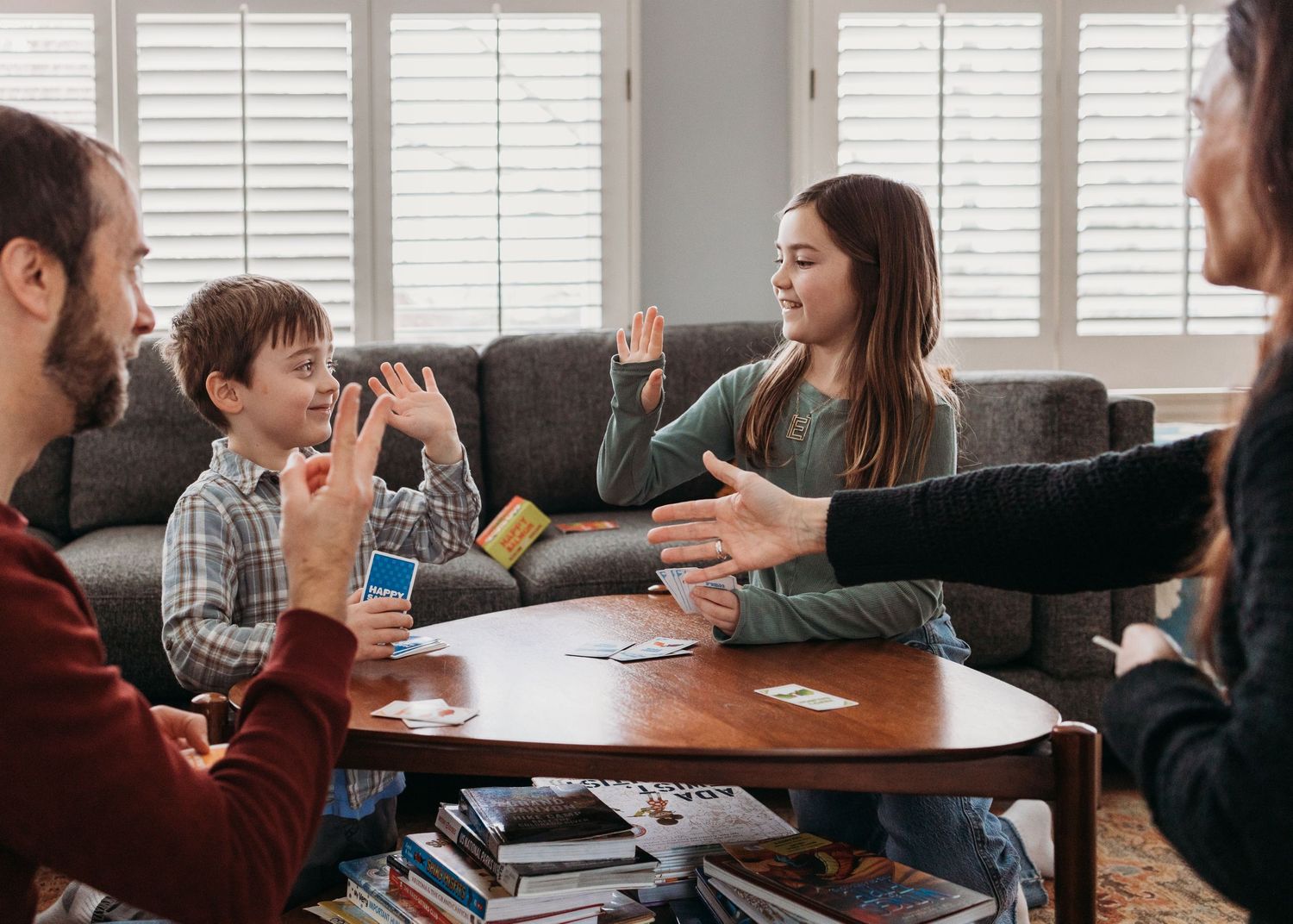 Family playing a card game together around a wooden coffee table in a cozy living room.
