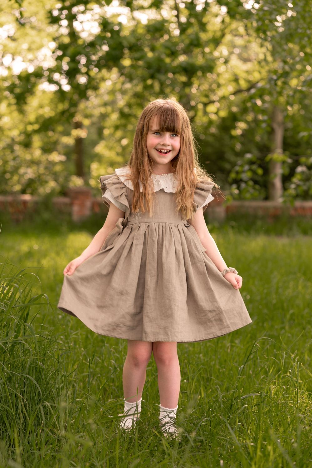 Happy girl standing in green grass field, smiling outdoors in natural sunlight during childhood photoshoot in Lincolnshire.