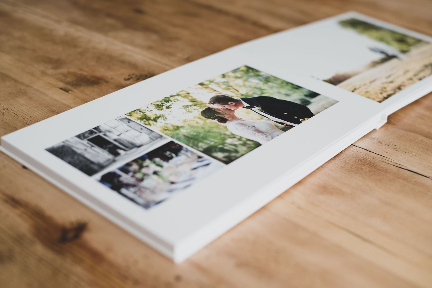 A white wedding photo album open on a wooden table displaying elegant collage of professional wedding photographs.