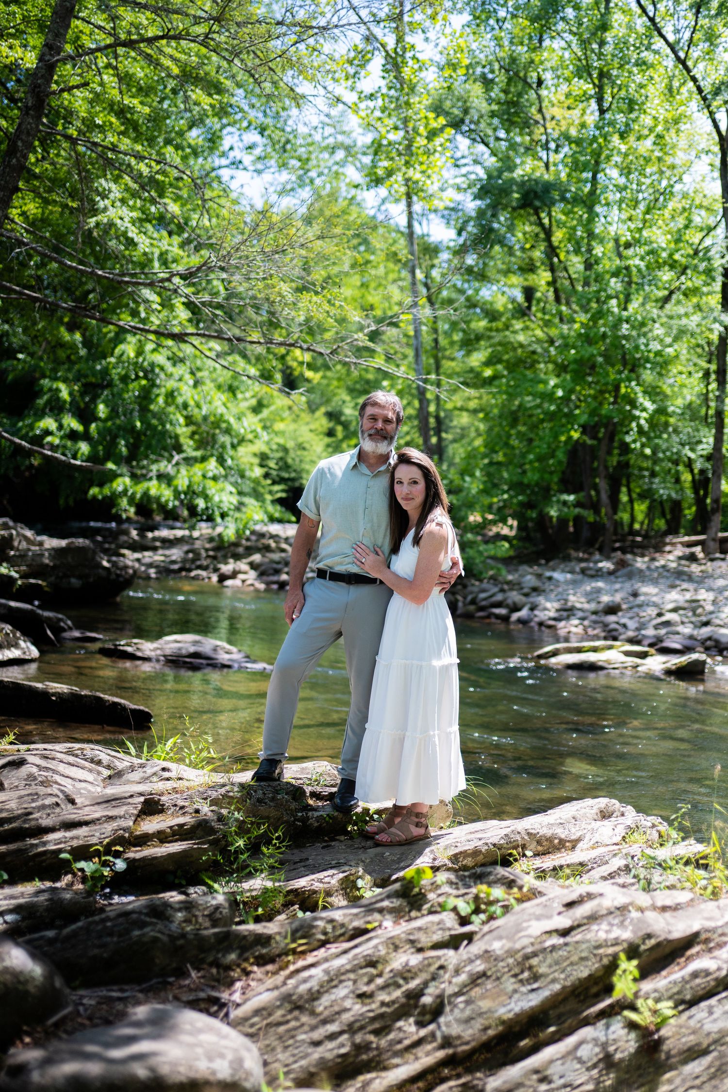 A bride and groom share a romantic moment on a mossy forest path surrounded by lush green trees.