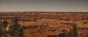 Vast panoramic view of an arid red rock canyon landscape stretching to the horizon at sunset.