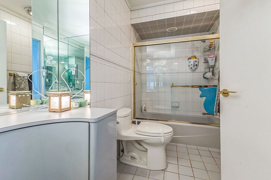 White tiled bathroom with vanity mirror, toilet, and gold-framed glass shower-tub combo with decorative accents.