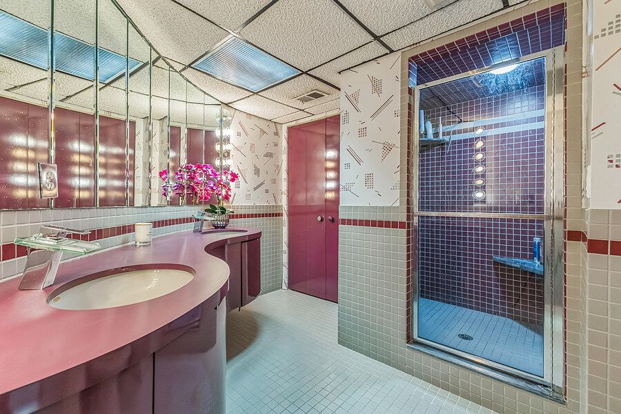 Retro pink bathroom with mirrored walls, curved vanity, tiled shower, and decorative wallpaper accents.