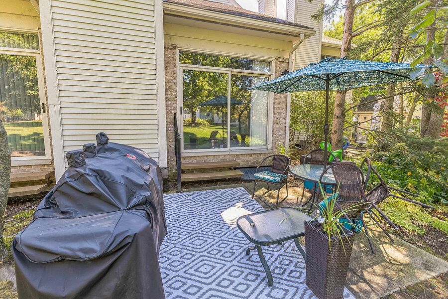 Cozy outdoor patio with patio furniture, umbrella, covered grill, and lush greenery surrounding the space.