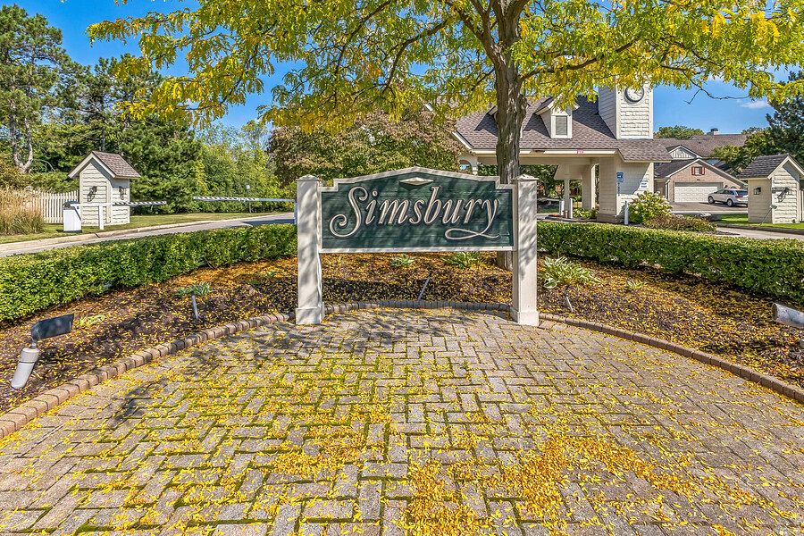 Brick entrance sign for Simsbury community surrounded by lush trees and manicured shrubs on a sunny day.