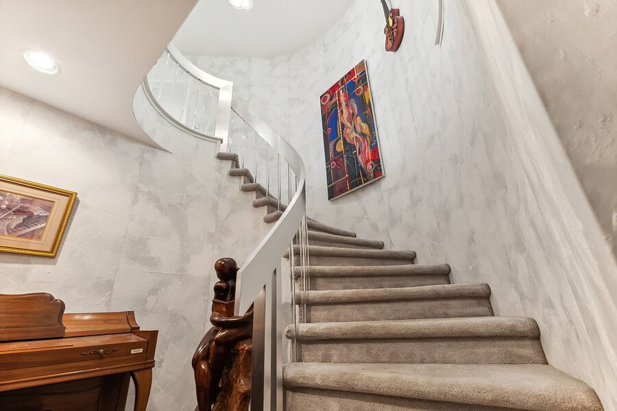 Elegant curved staircase with white railing, marble walls, and carpeted steps in a luxury home foyer.