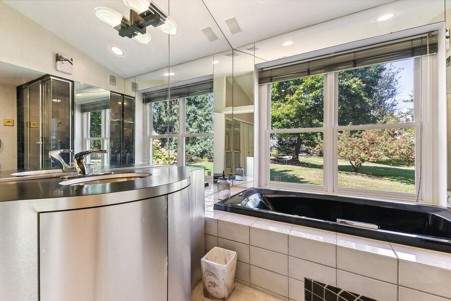 Modern bathroom with black soaking tub, large windows overlooking lush garden, and sleek stainless steel vanity.
