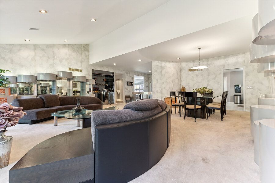 Spacious open-plan living room with curved dark sofas, mirrored walls, neutral carpet, and elegant dining area in background.