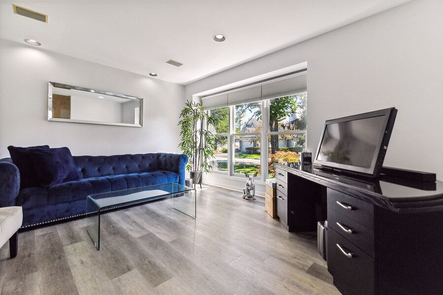 Bright modern living room with blue velvet sofa, glass coffee table, hardwood floors, and large sliding glass doors.