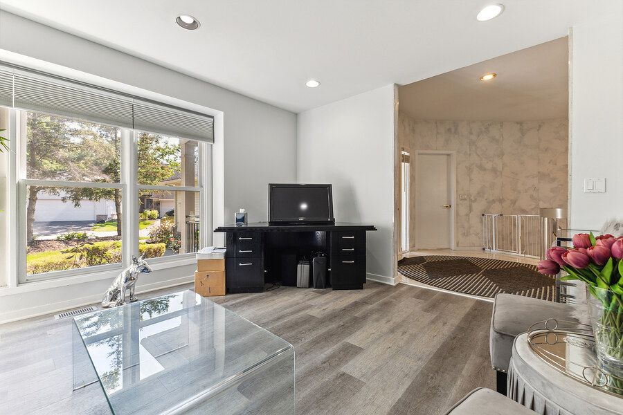 Bright living space with hardwood floors, large window, black desk, and view of a jacuzzi tub area.