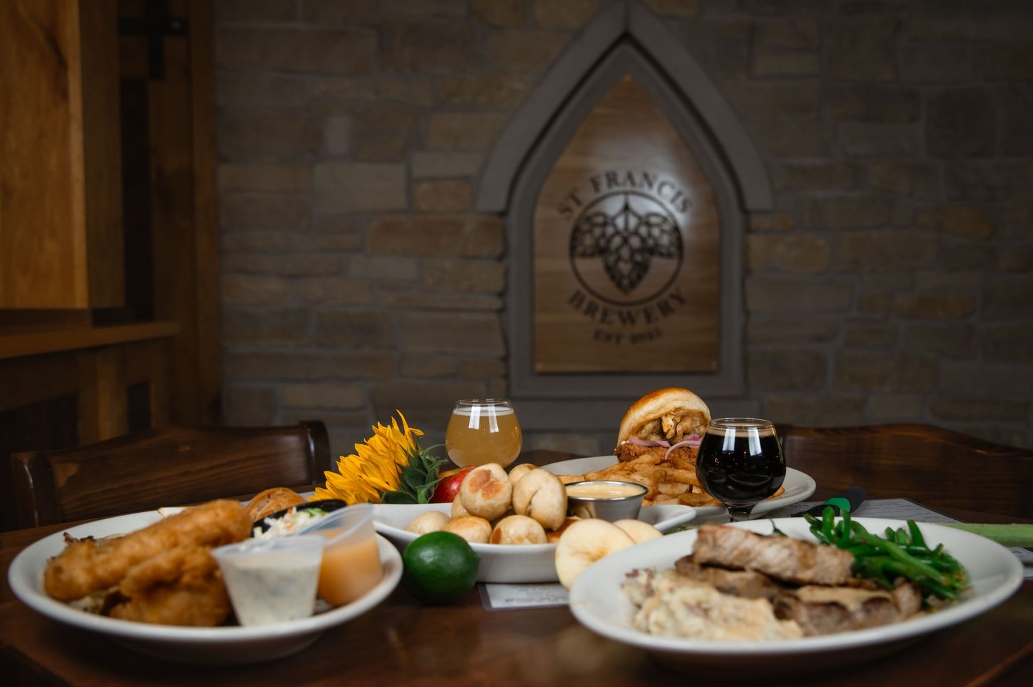 St. Francis Brewery spread featuring craft beers, artisan bread, cheese, and entrees on white plates in a rustic stone interior.