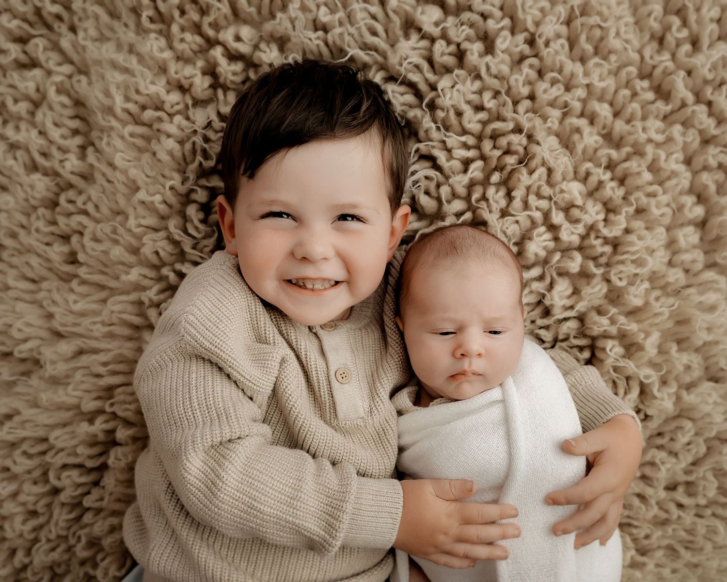 sibling cuddling newborn baby during portrait session