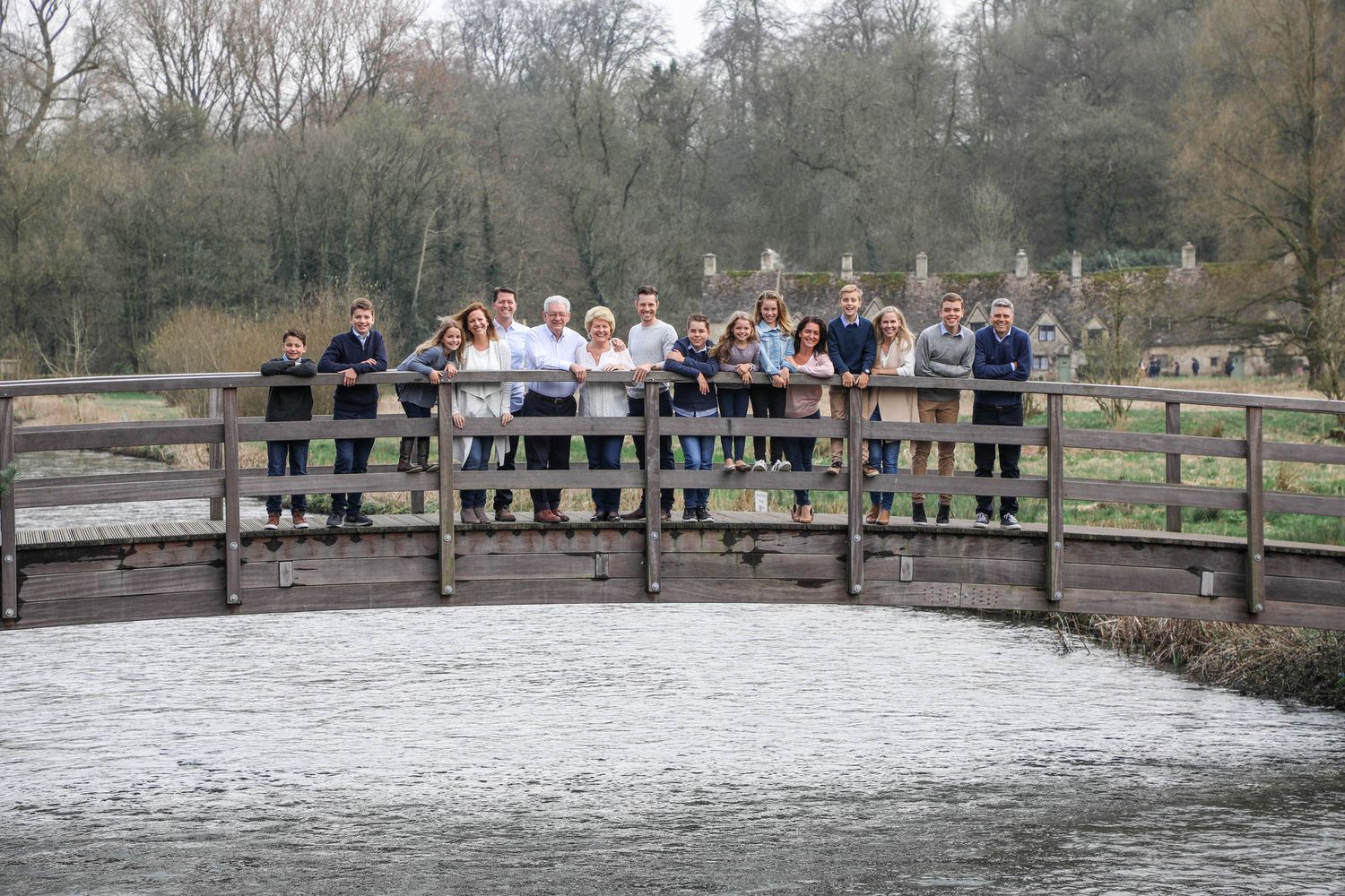 Large family group posing together on a wooden bridge over a river in a scenic park setting.