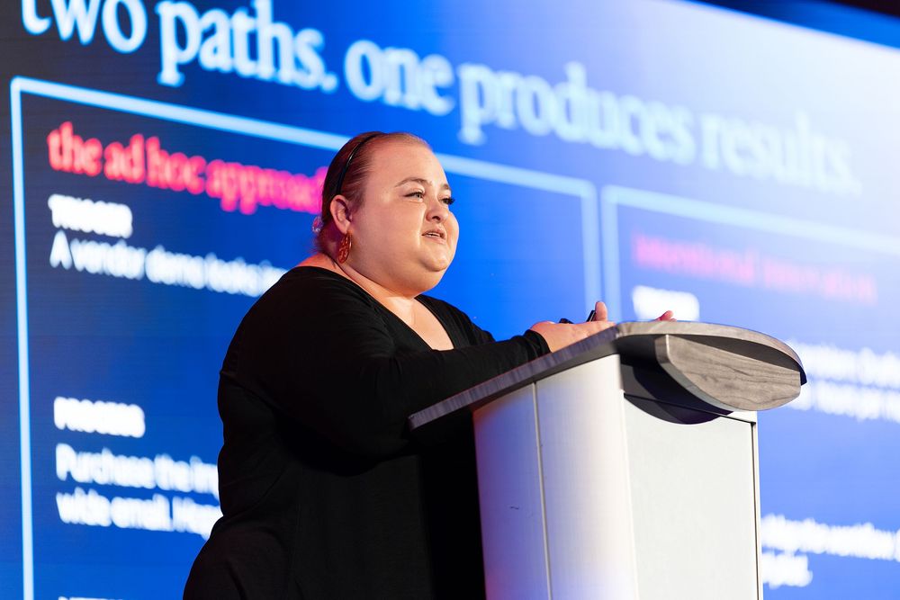 Professional woman speaker presenting at a business conference podium with a slide about ad hoc approaches.