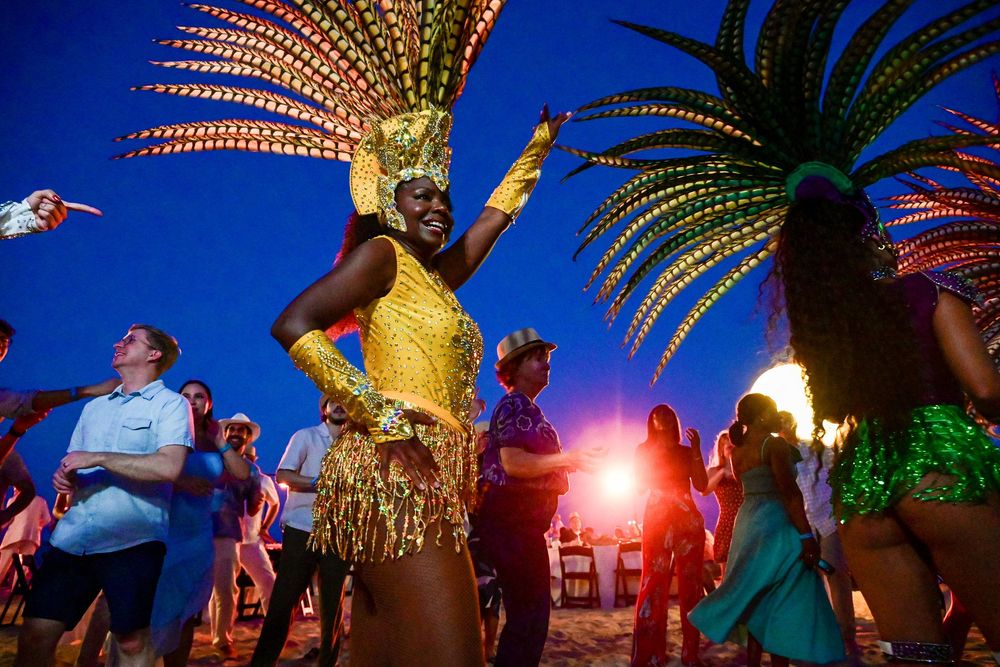 Vibrant carnival dancer in golden costume with feathered headdress performing at a beach party at dusk.