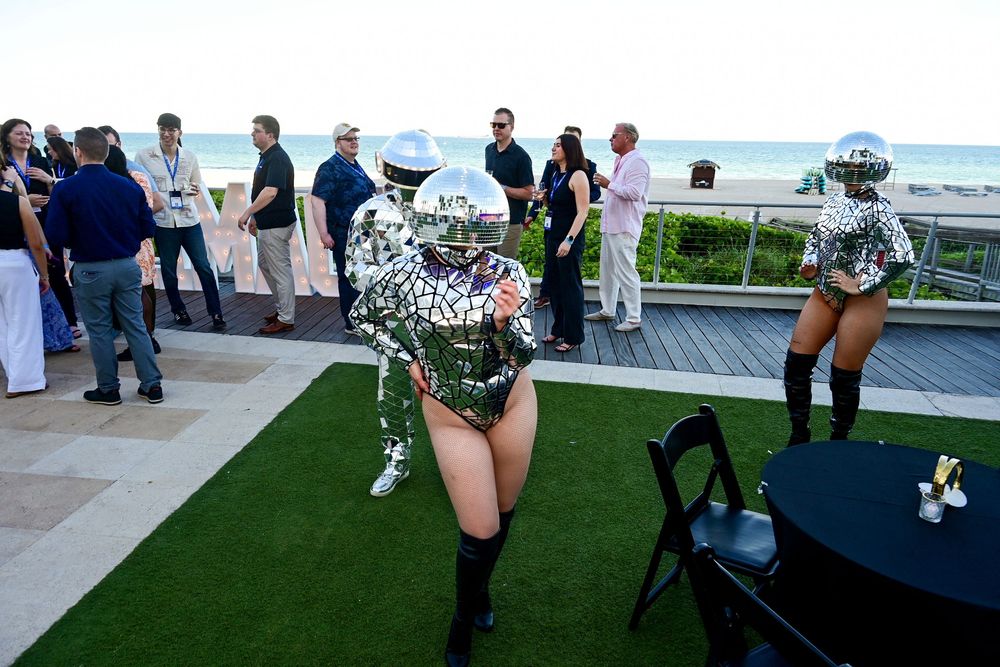 Performers in mirrored disco ball costumes entertain guests at an outdoor beachside event party.