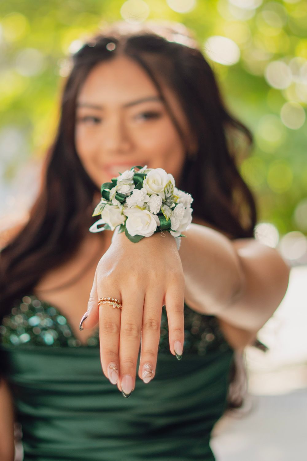 Young woman in green prom dress showing off a white floral wrist corsage to the camera.