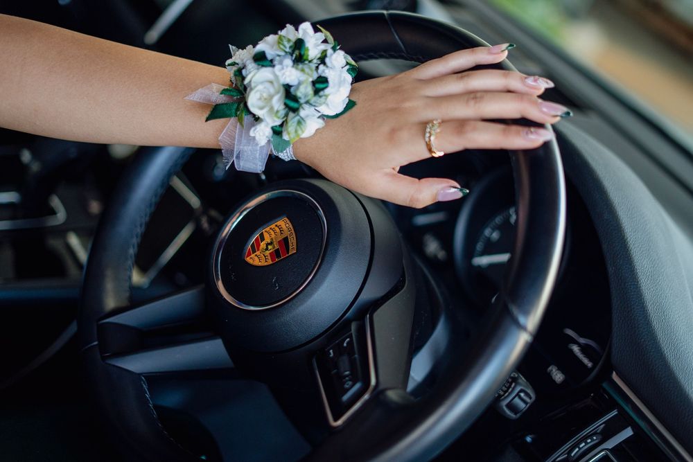 Close-up of a woman wearing a floral wrist corsage while holding a Porsche steering wheel.