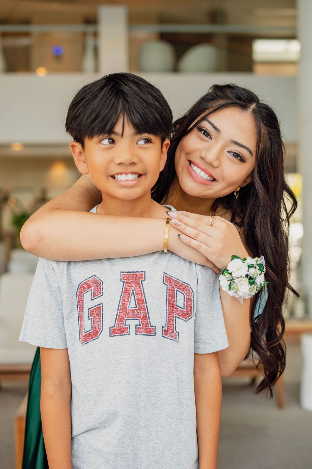 Smiling young woman in green prom dress with corsage hugging a young boy in a GAP shirt.