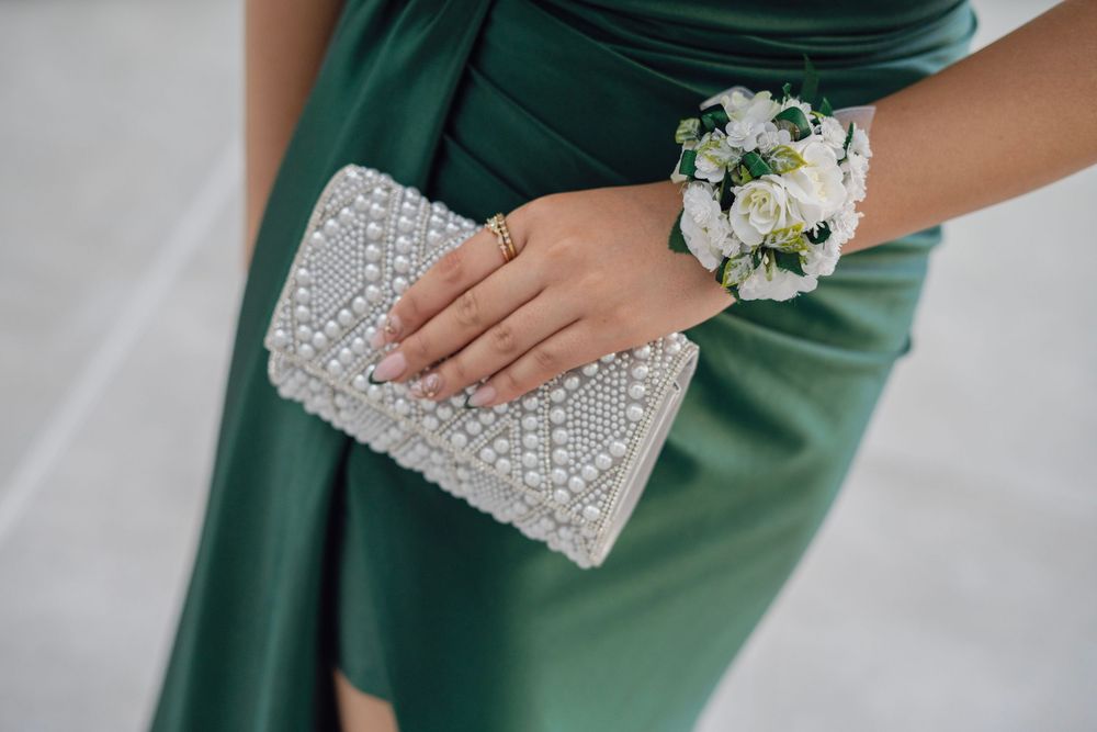Close-up of a woman in a green satin dress holding a pearl clutch with a floral wrist corsage.