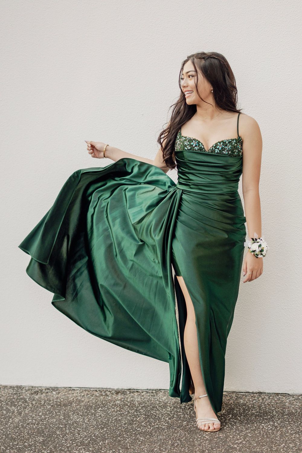 Young woman in a stunning emerald green satin gown with a thigh-high slit poses gracefully.