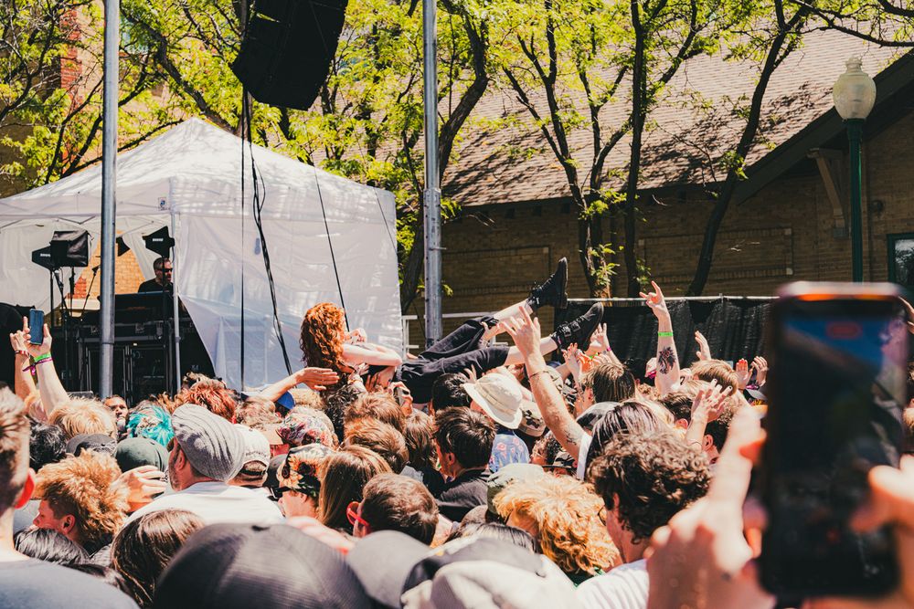 Energetic outdoor music festival crowd with stage diver surfing over fans near a white tent stage.