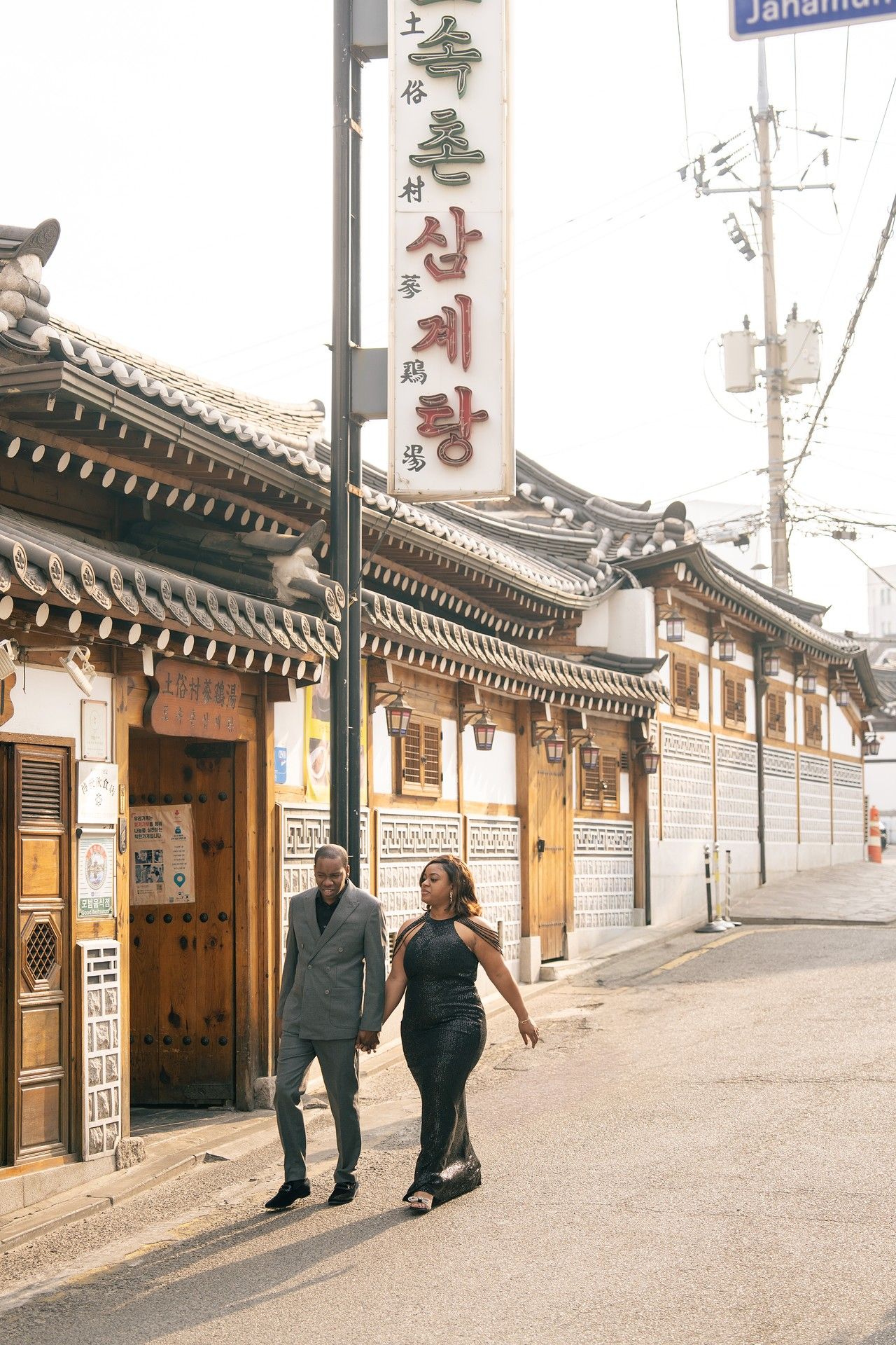 Couple walking past traditional Korean hanok buildings on a quiet street in Seoul, South Korea.
