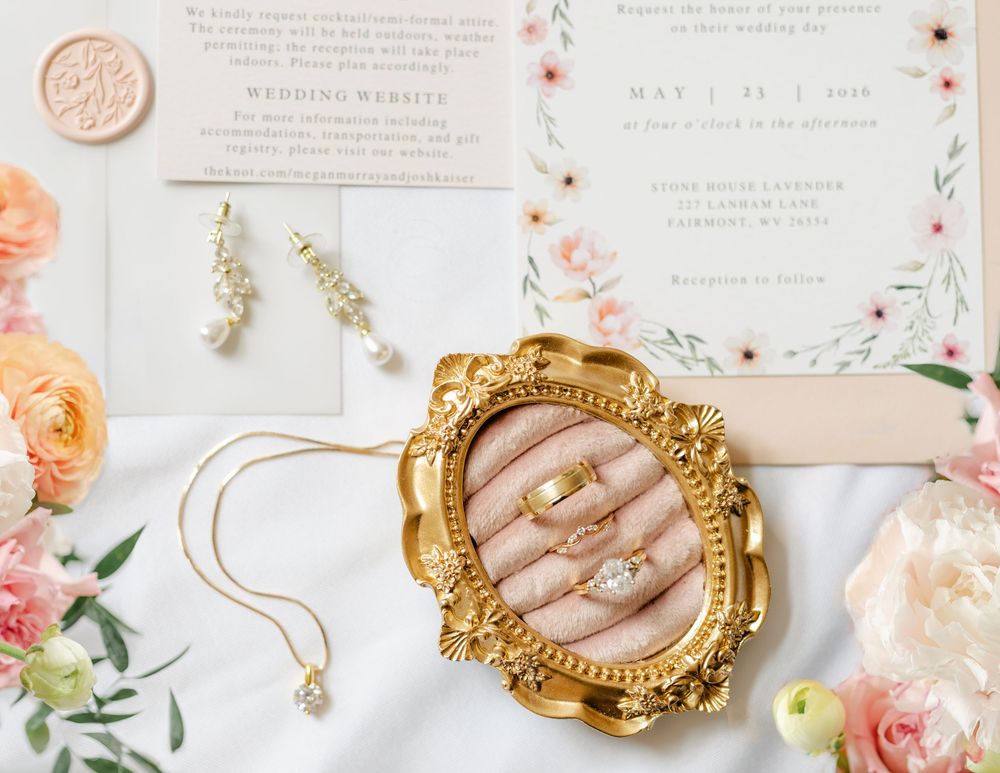 Wedding flat lay with gold ring dish, floral invitations, pearl earrings, and pink roses.