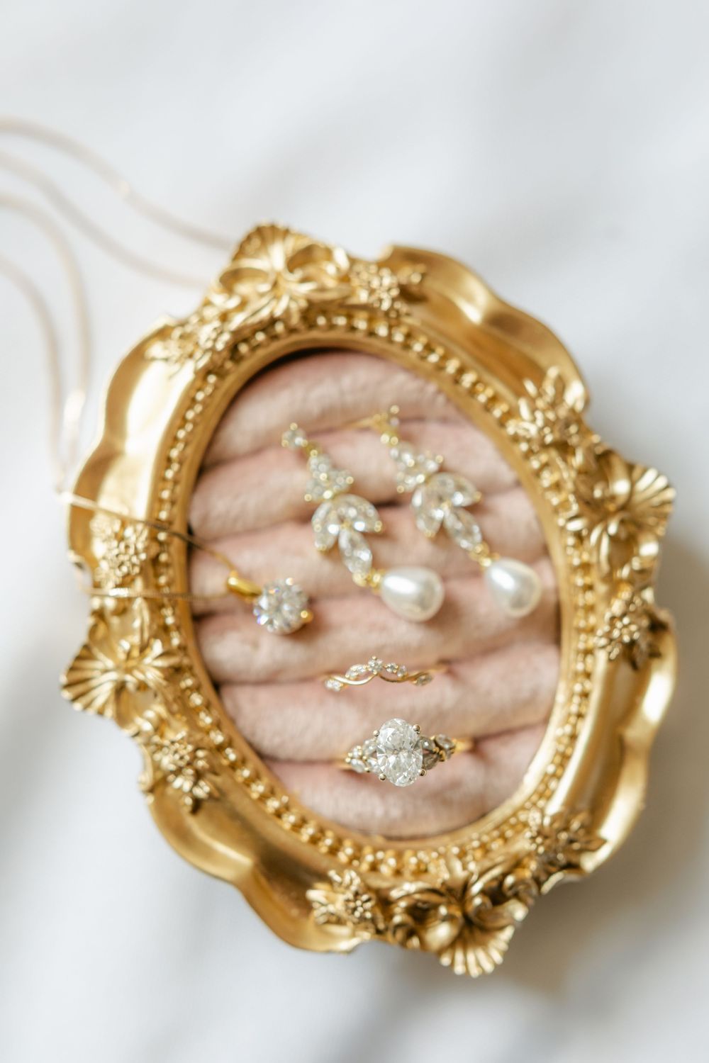 Close-up of gold ornate jewelry dish with diamond engagement ring and floral drop earrings.