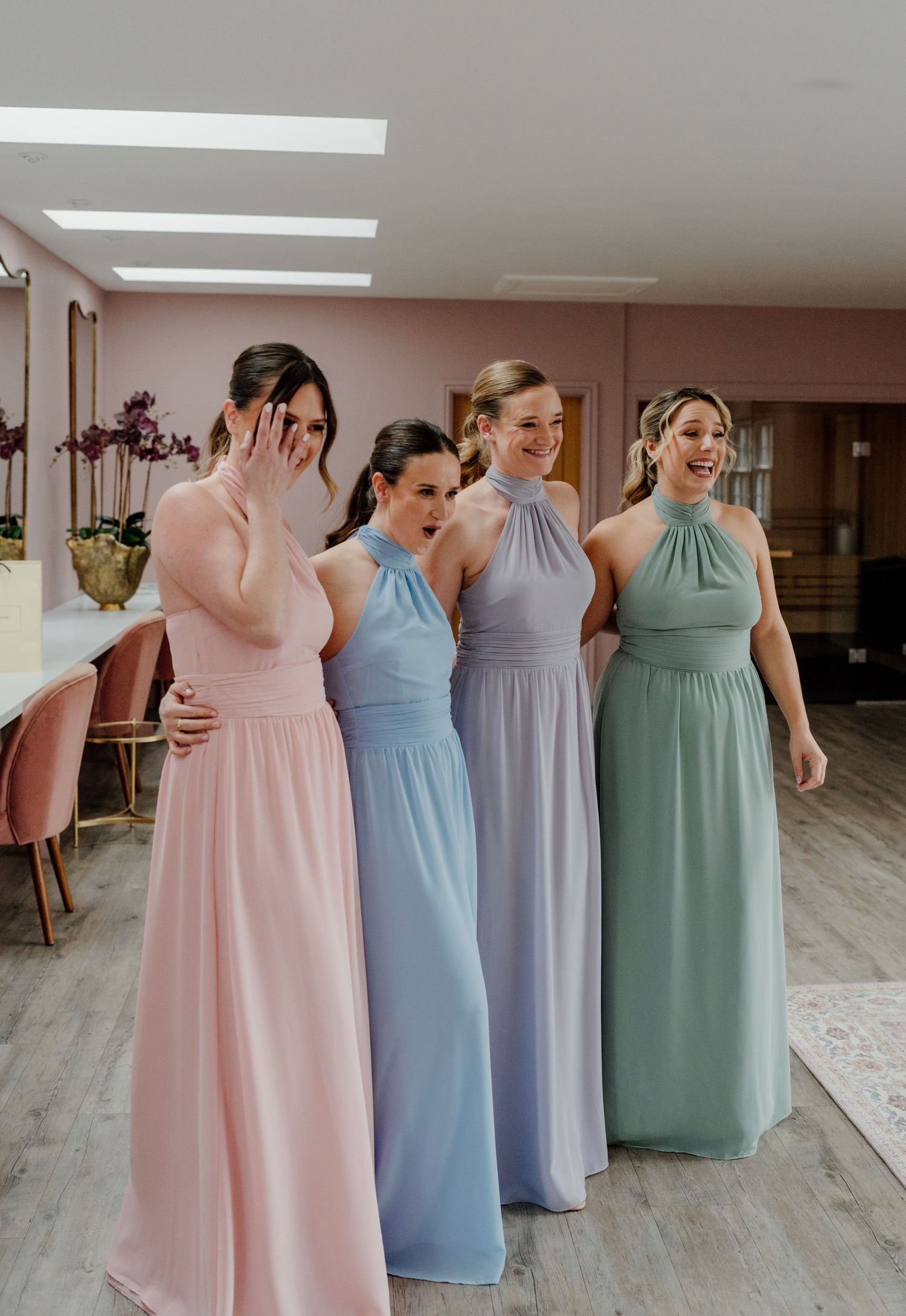 Four bridesmaids in pastel gowns laughing together during bridal first look at quantock lakes.