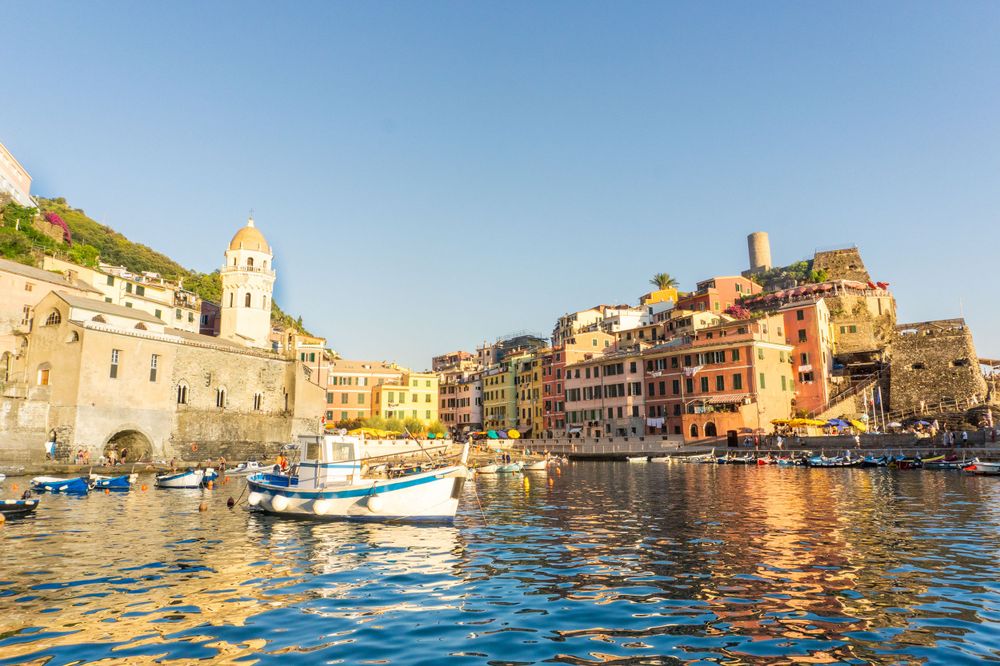 Vernazza harbor at sunset with colorful buildings reflecting in the Mediterranean waters.