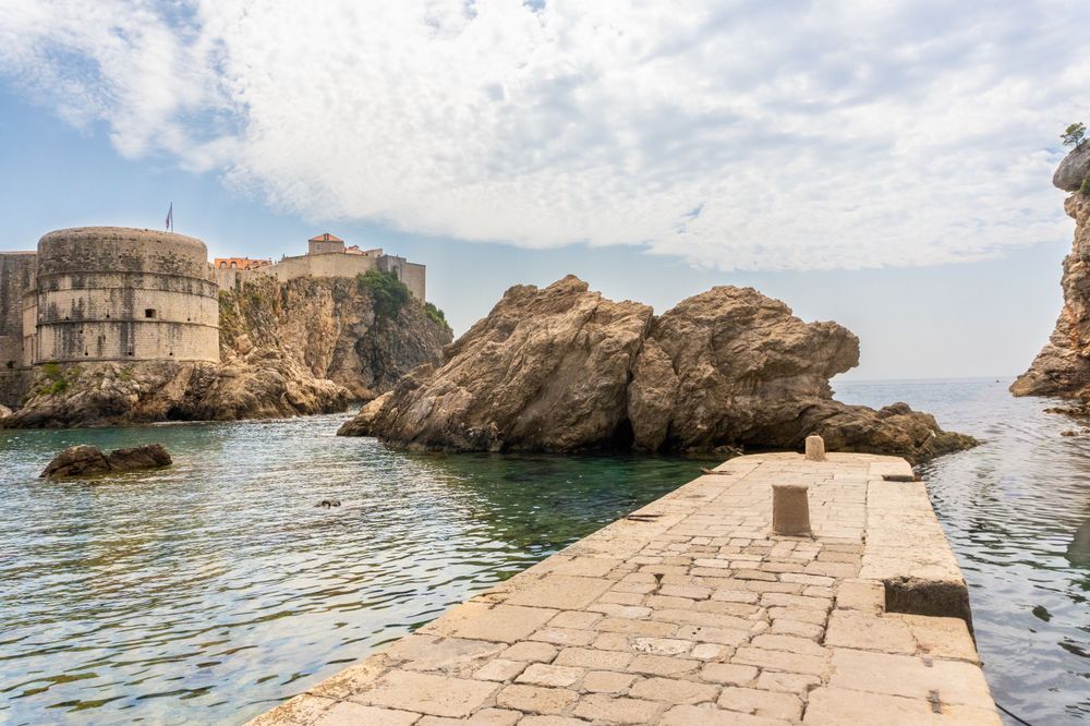 Stone pathway along fortress walls in Dubrovnik with rocky coastline and Adriatic Sea.