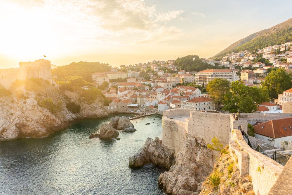 Golden sunset illuminates coastal cliffs and buildings along Dubrovnik's dramatic shoreline.